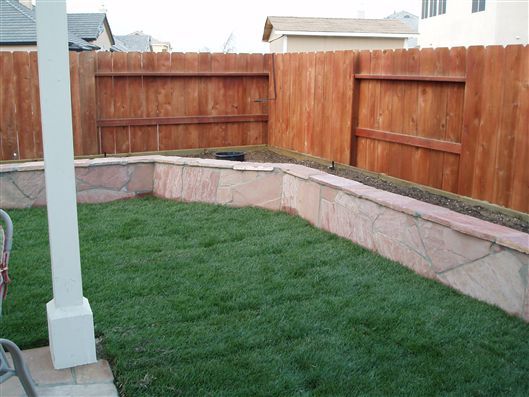 Backyard lawn with a curved stone retaining wall and wooden privacy fence