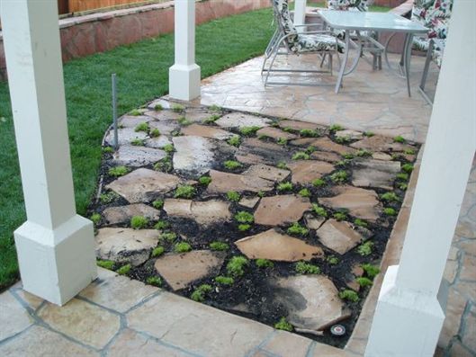 Stone garden path with black gravel between stepping stones beside a patio and white posts