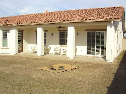 Single-story house with a tiled roof, white columns, and a front porch with chairs.