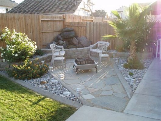 Backyard patio with stone seating area, white chairs, fire pit, and palm tree