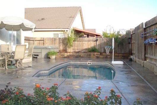 Backyard swimming pool with patio furniture, umbrella, fence, and flower bed on a sunny day