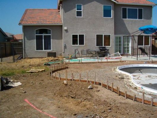 Backyard with unfinished pool, dirt yard, and a two-story house with patio furniture