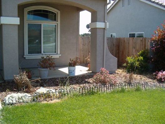 Front yard with green lawn, stone border, porch columns, and a window beside landscaped shrubs