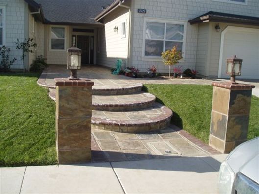 Front yard stone steps and walkway leading to a house entrance, flanked by brick pillars and lawn lanterns