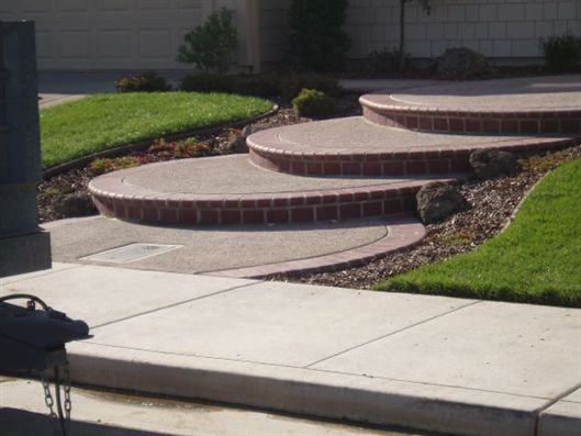 Curved concrete steps beside a sidewalk and green lawn in front of a building