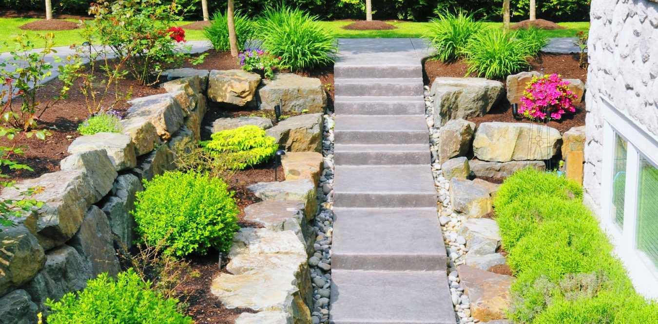 Stone garden steps between rock walls and green shrubs leading up a landscaped yard