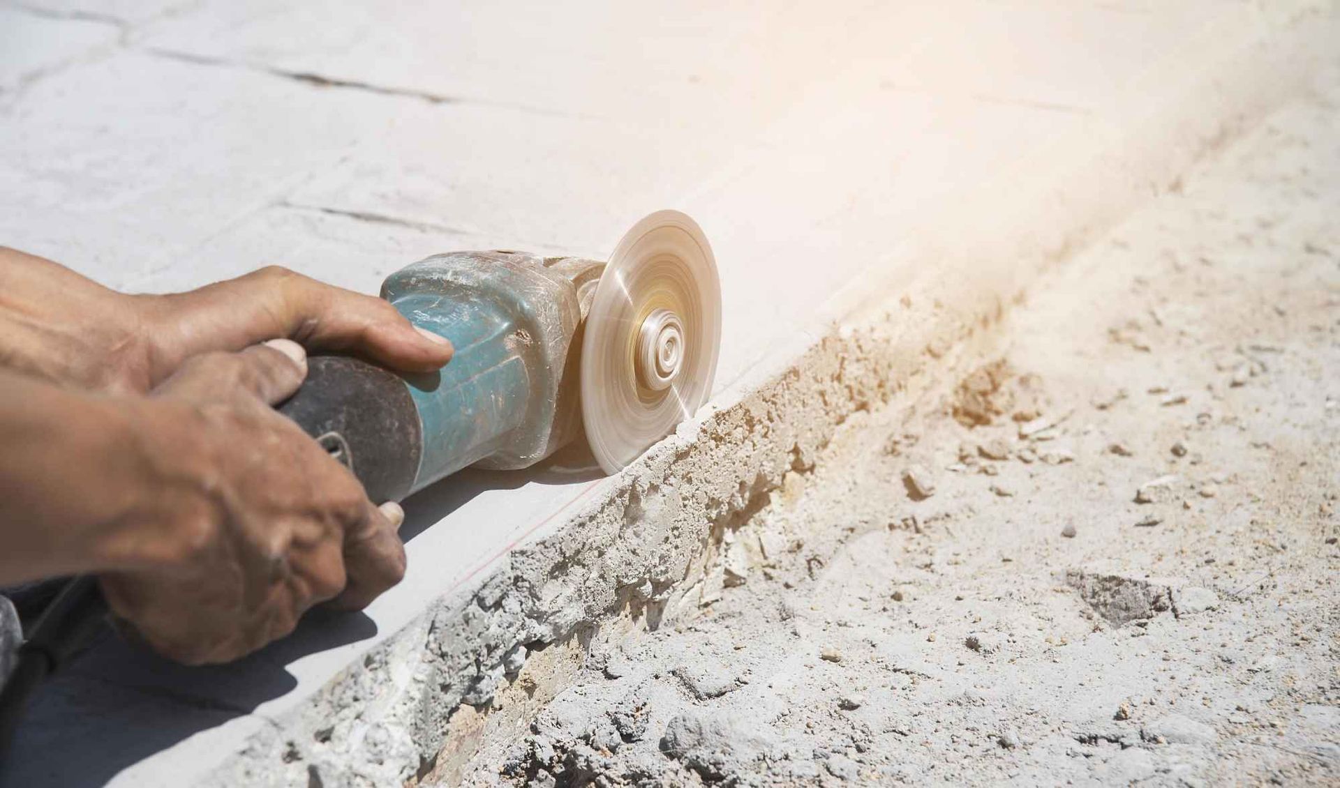 Hands use a blue angle grinder to smooth a concrete edge, creating dust.