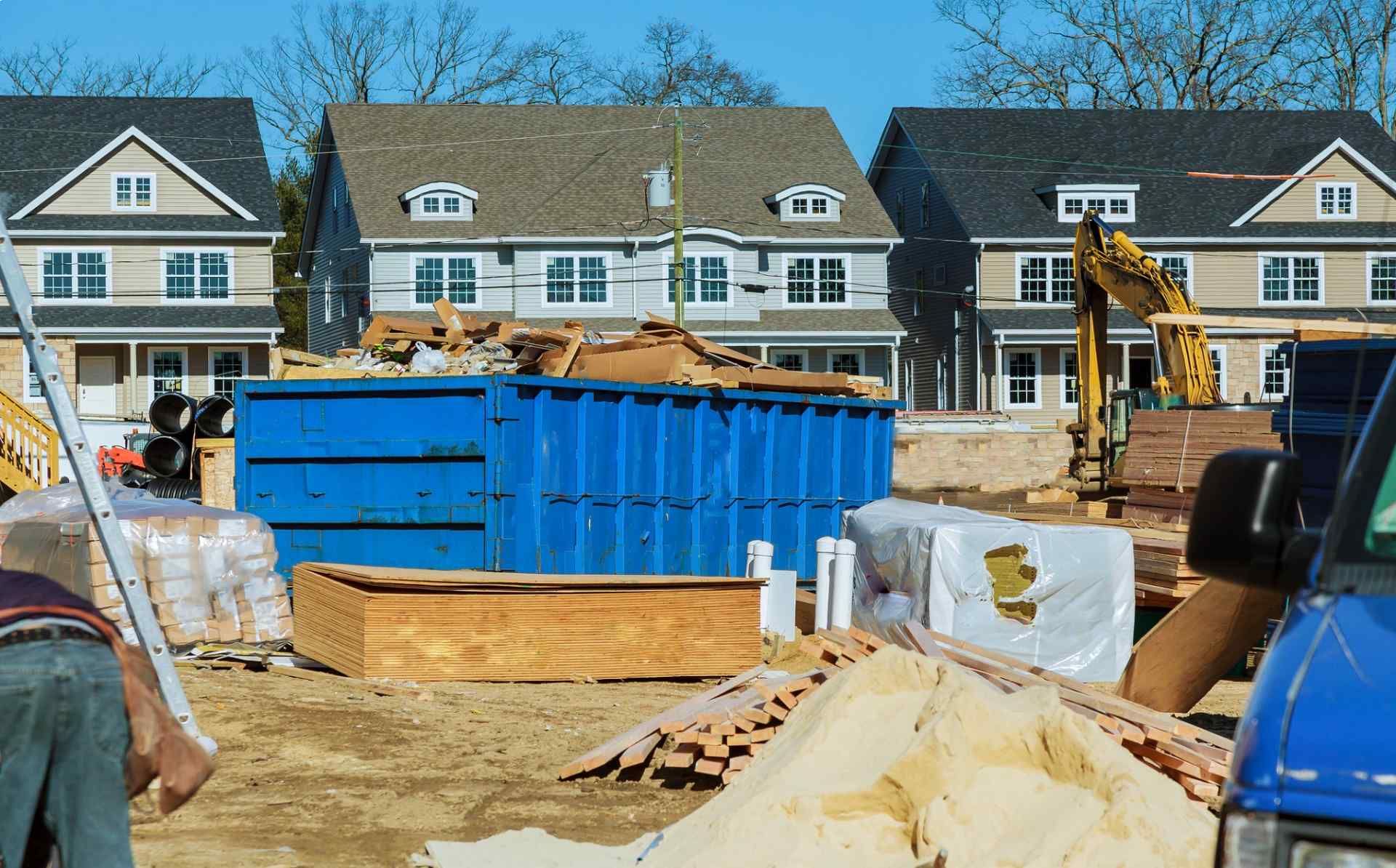 Construction site with blue dumpster and machinery in front of row houses
