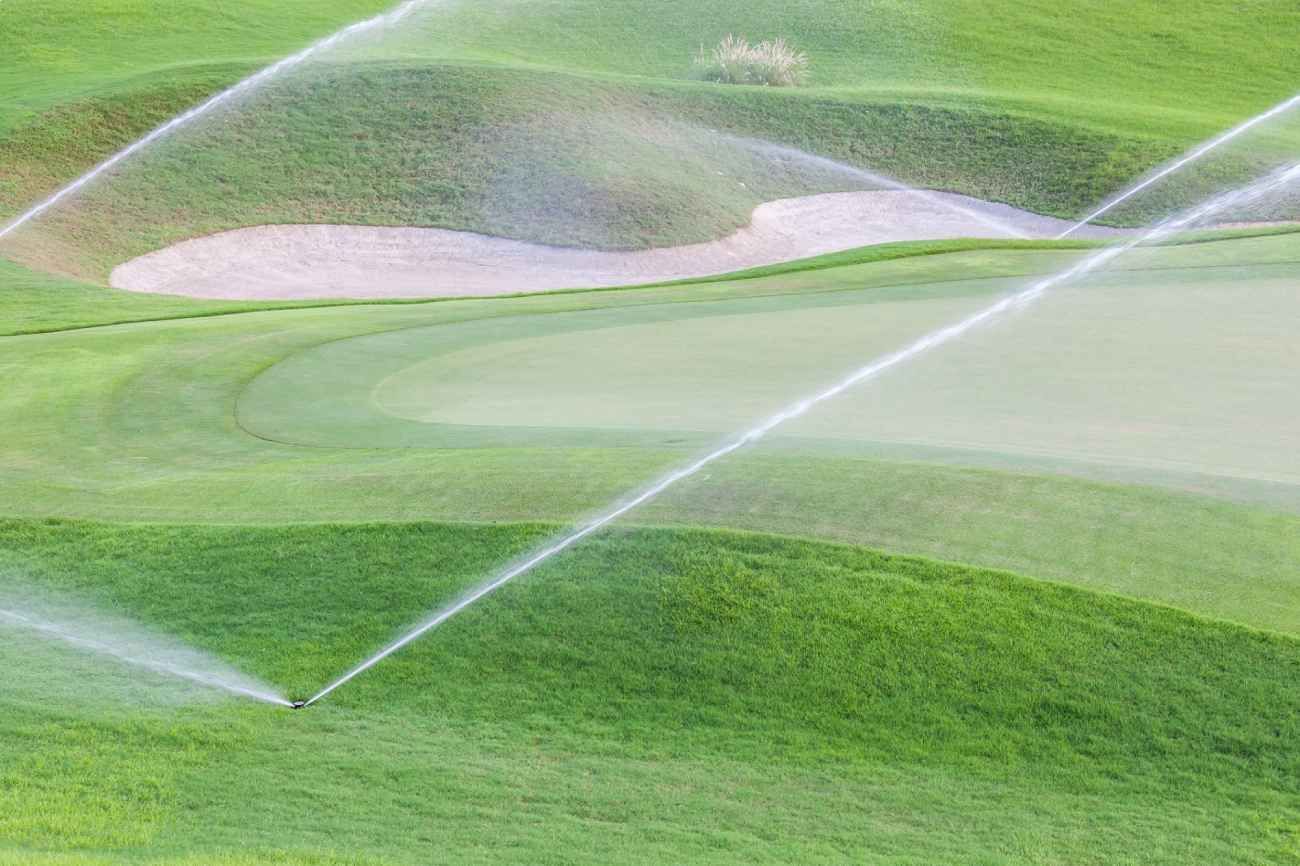 Sprinklers watering a lush green golf course with sand bunkers.