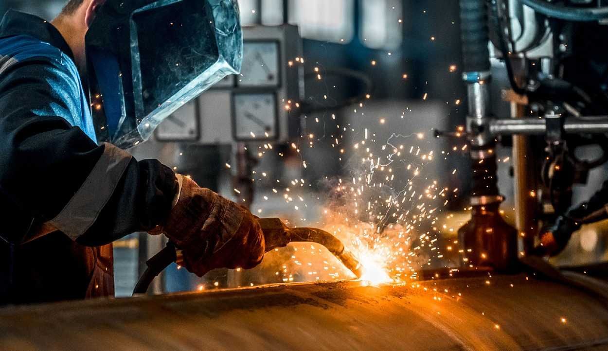 Welder in protective gear sparks metal workpiece in an industrial workshop