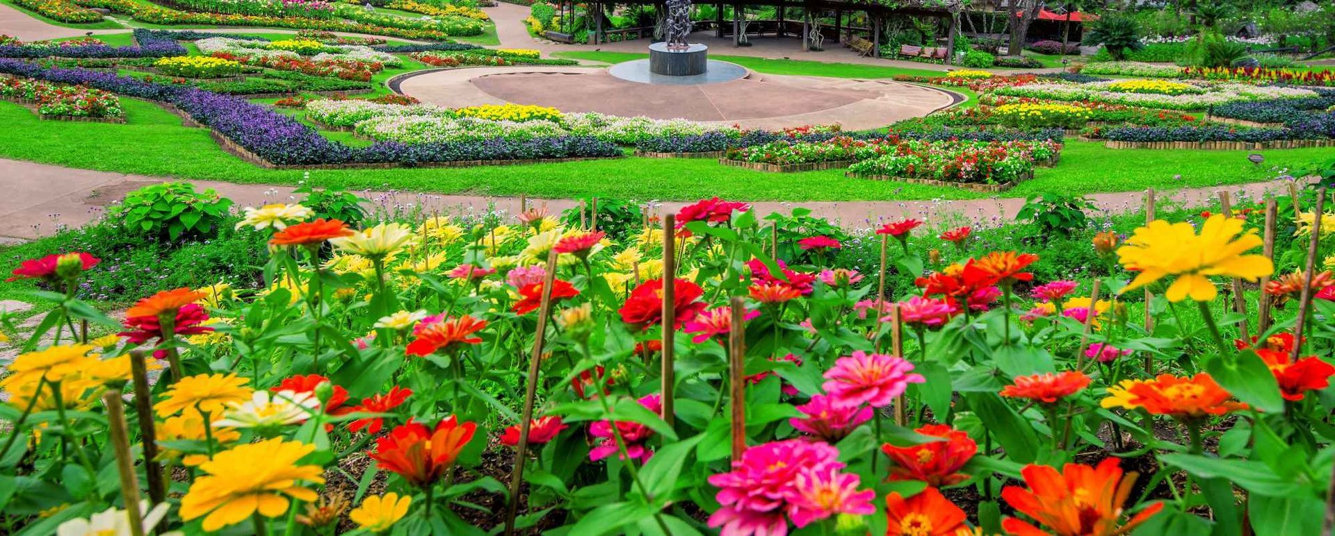 Colorful flower garden with red, pink, yellow, and orange blooms in layered beds along a landscaped path