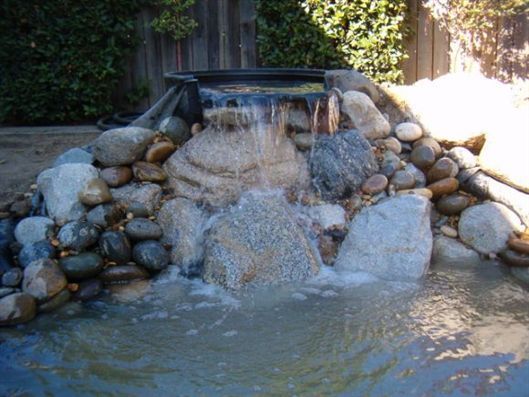 Small waterfall spilling over rocks into a shallow pond in a landscaped garden
