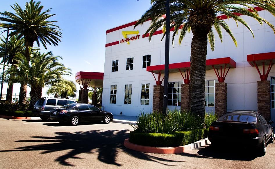 Modern building with red awnings, palm trees, and parked cars in bright sunlight
