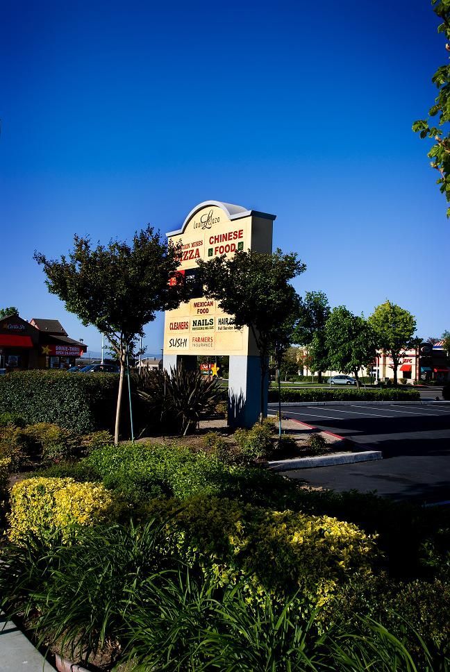 Shopping center sign beside a landscaped parking lot under a clear blue sky