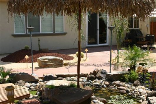 Desert-style backyard with rocks, small plants, and a patio in front of a house.