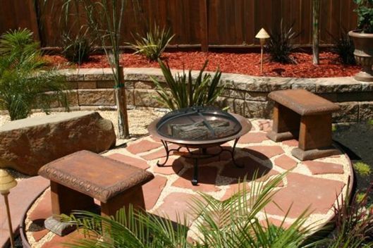 Patio fire pit surrounded by stone benches and potted plants in a landscaped garden