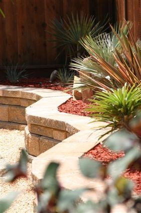Curved stone pathway through a desert garden with agave and red gravel beside a wooden fence