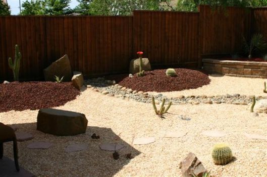 Zen-style garden with gravel, rocks, and low shrubs beside a wooden fence.