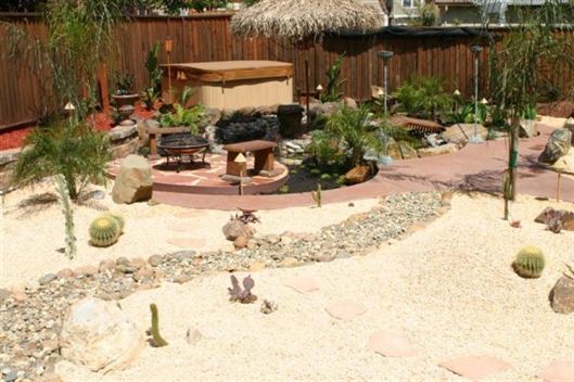 Desert-style backyard patio with rocks, succulents, a fire pit, and a thatched gazebo behind a wooden fence