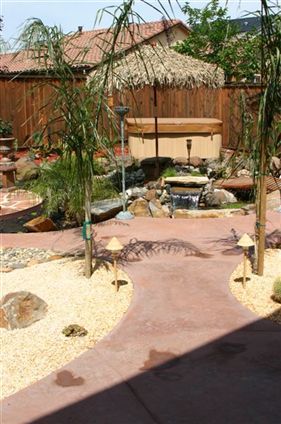 Backyard garden path with desert plants, rocks, a bench, and a thatched gazebo under sunny light