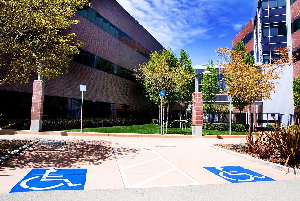 Accessible parking spaces in front of a modern office building with trees and brick walls