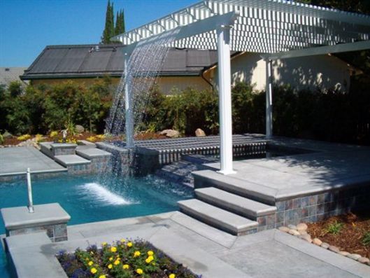 Backyard pool with a pergola-style waterfall spilling into the water and surrounding patio steps