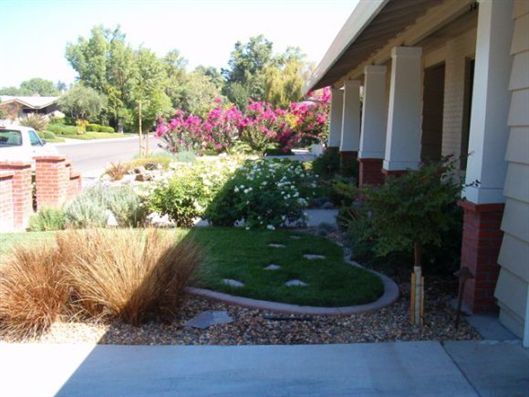 Landscaped front yard with shrubs, pink flowers, and a house porch along a curved walkway.