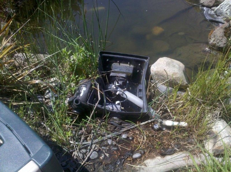 Broken black device on grassy riverbank beside water and rocks