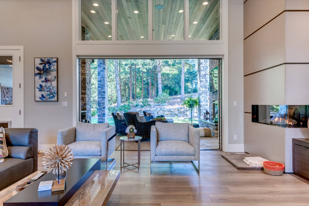 Modern living room with a large sliding glass door opening to a patio, fireplace, and two light gray armchairs.