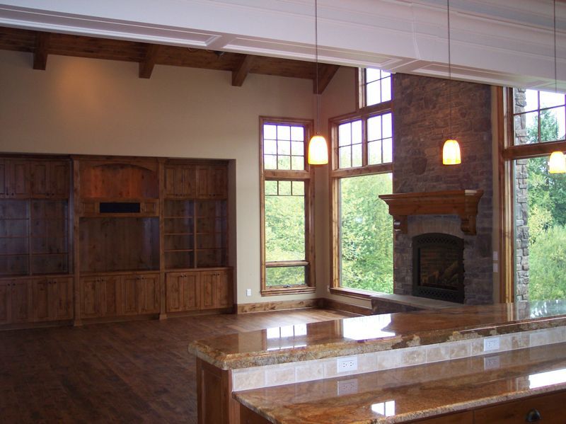 A spacious living room with dark wood cabinetry, a stone fireplace, and a granite-topped kitchen island.