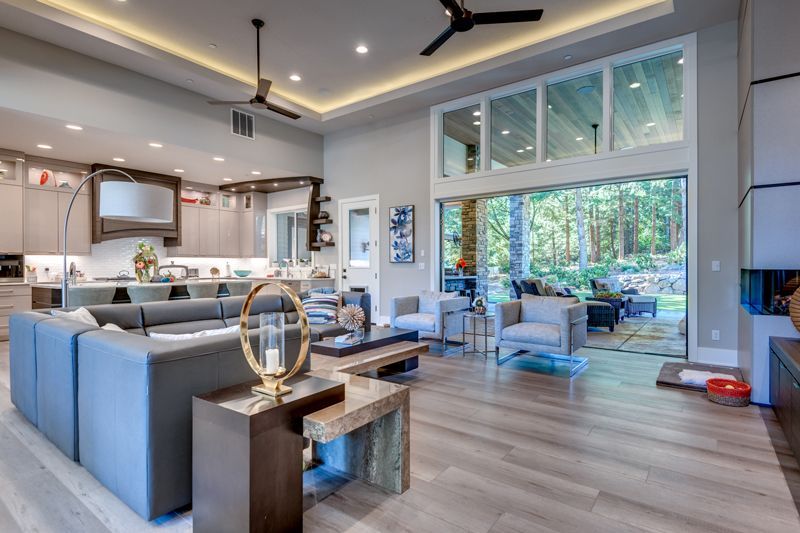 Open-plan living room with grey sectional sofa, wooden console table, and floor-to-ceiling windows looking onto a patio.
