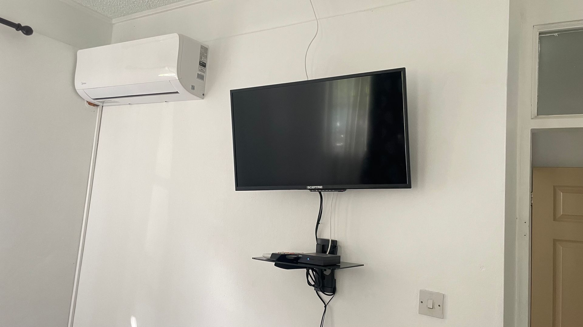 A flat screen tv is hanging on a wall next to an air conditioner.