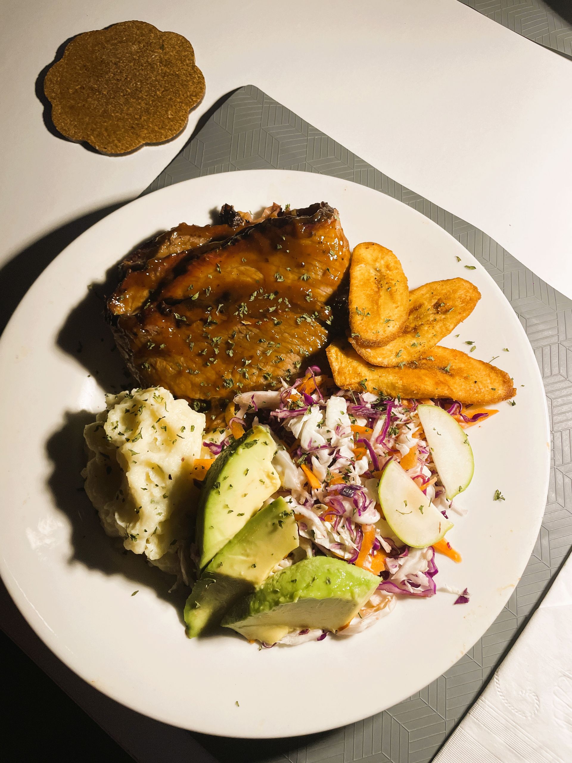 A plate of food with meat , potatoes , coleslaw and avocado on a table from V lounge Restaurant inside Villa copthall.