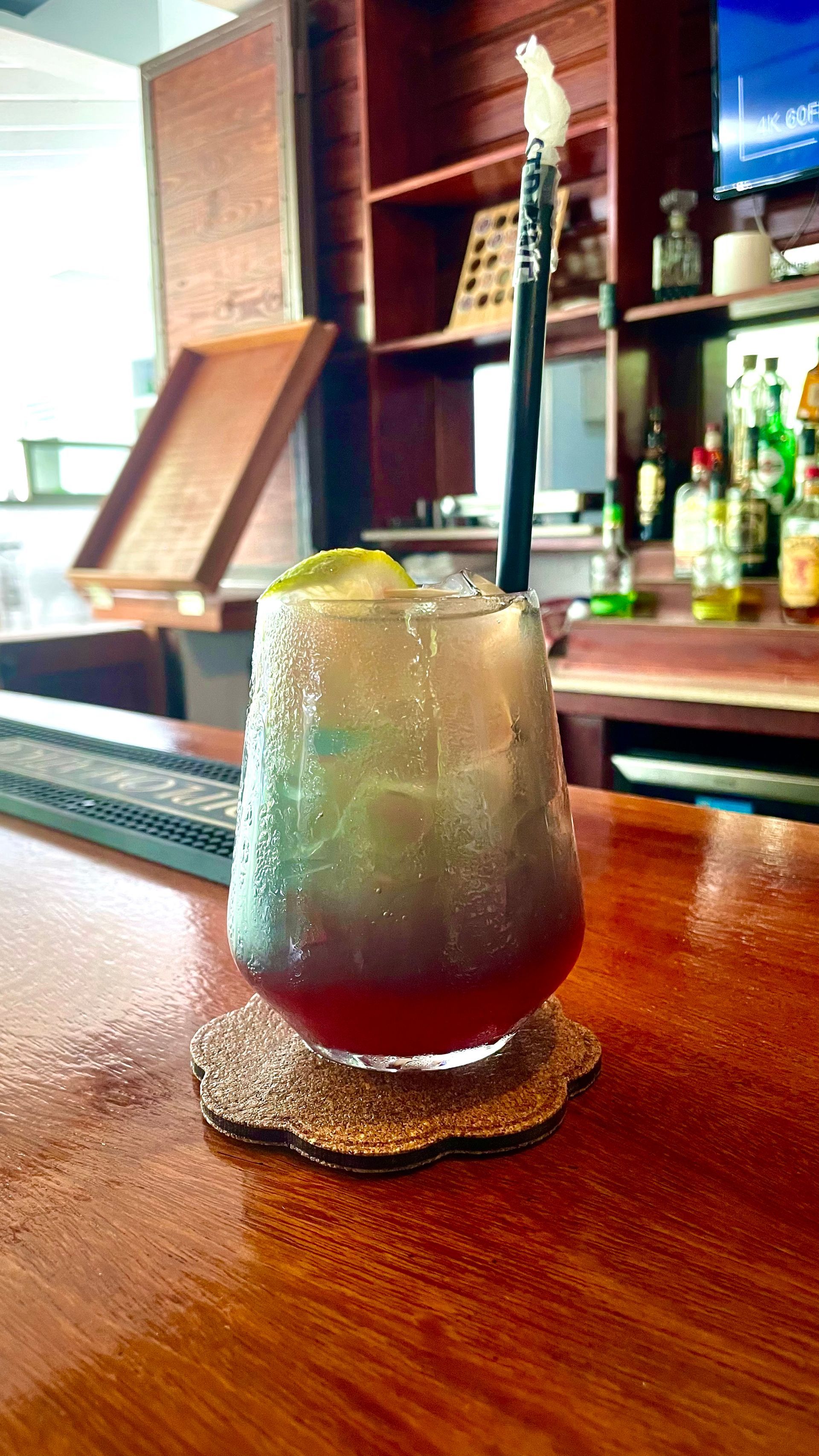 A drink with a straw in it is sitting on a wooden table  at V lounge Restaurant inside Villa copthall. 