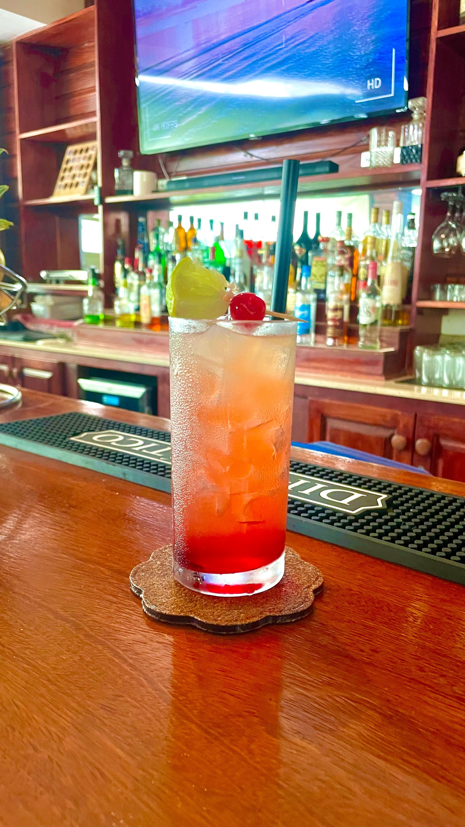A tall red drink with decor on top, at the bar  at V lounge Restaurant inside Villa copthall. 