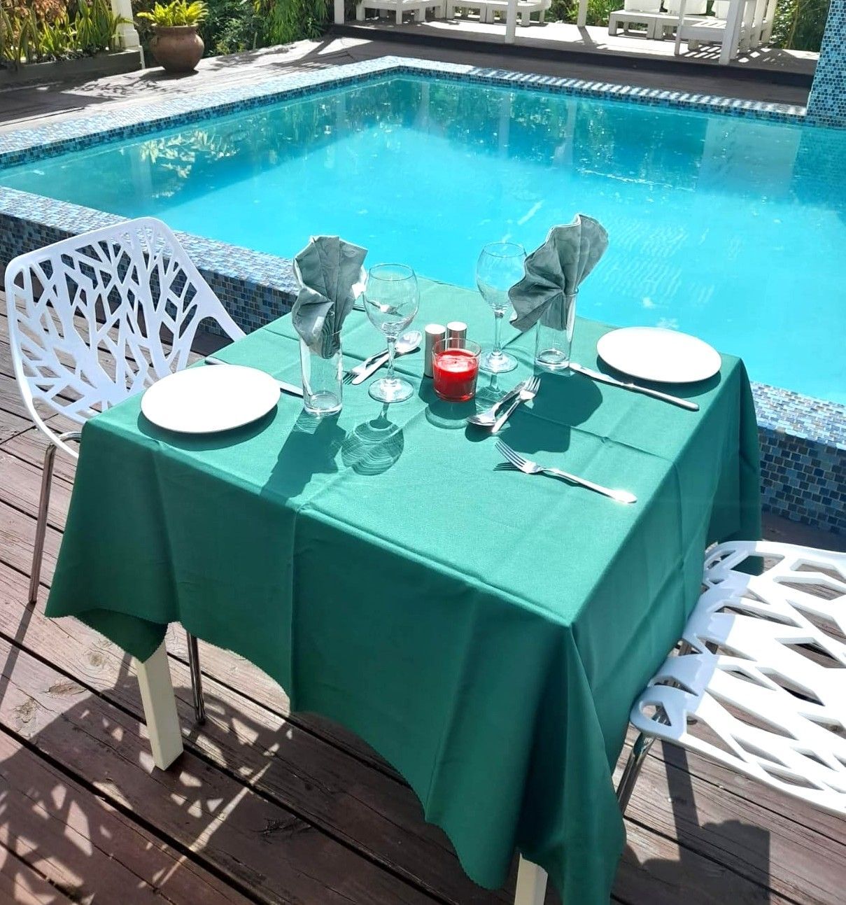 A table with plates and glasses on it in front of a swimming pool at Villa Copthall.