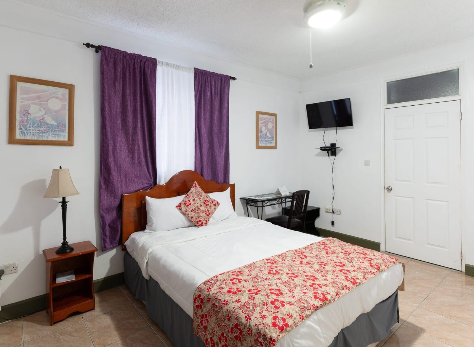 A hotel room with a bed , desk , lamp and television.
