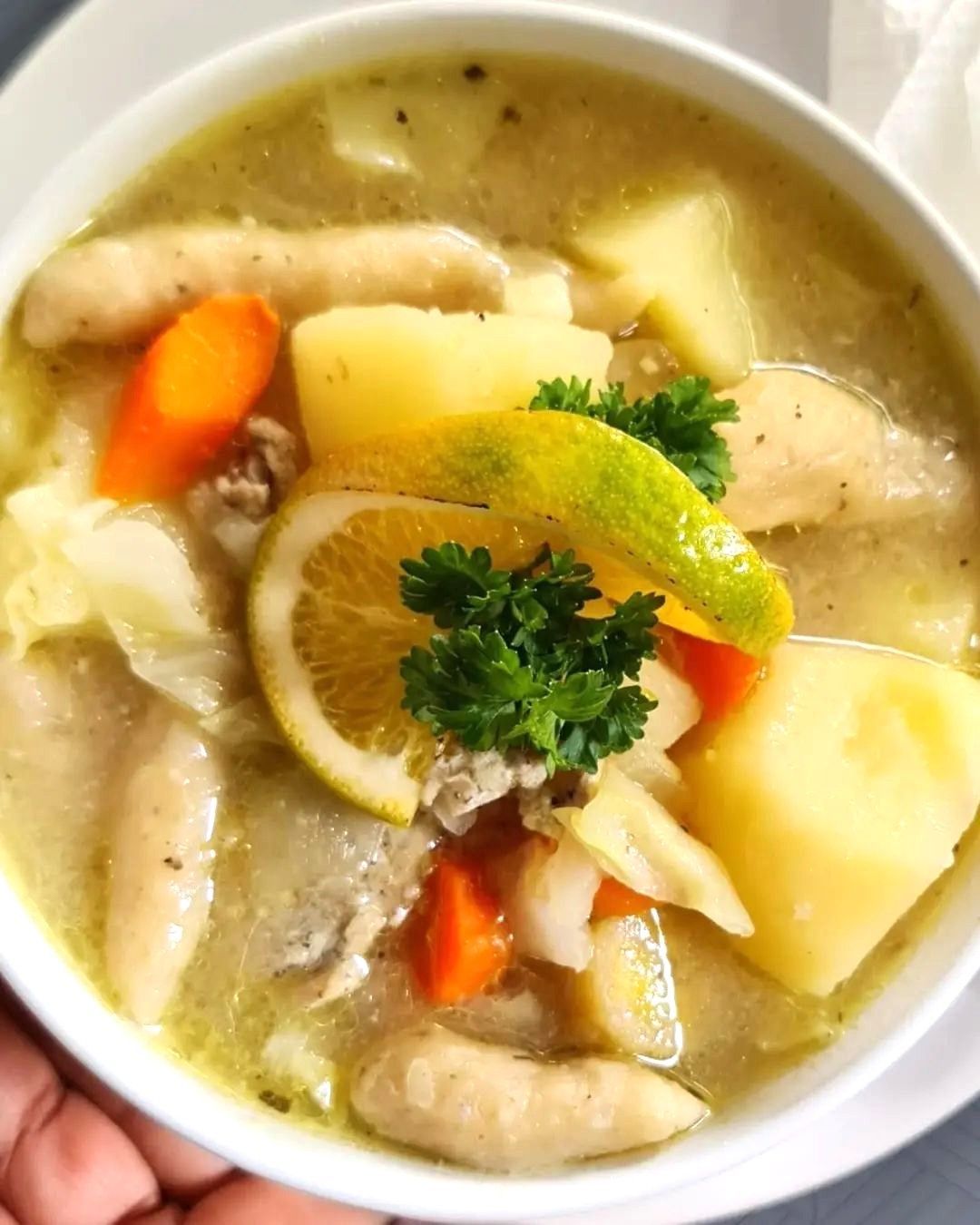 A bowl of soup with chicken , potatoes , carrots and lemon slices from V lounge Restaurant inside Villa copthall.