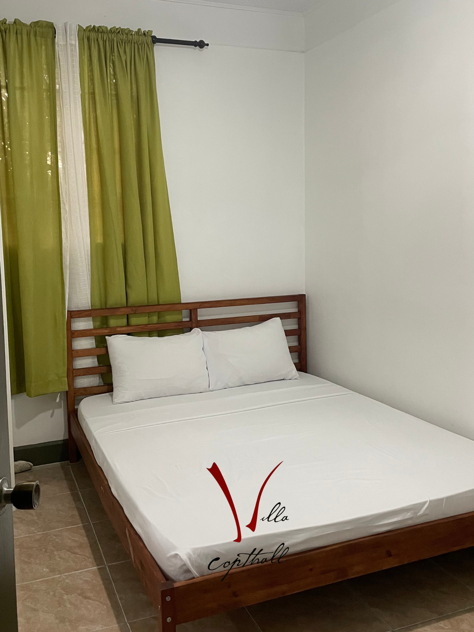 A bed with white sheets and pillows in a room with green curtains.