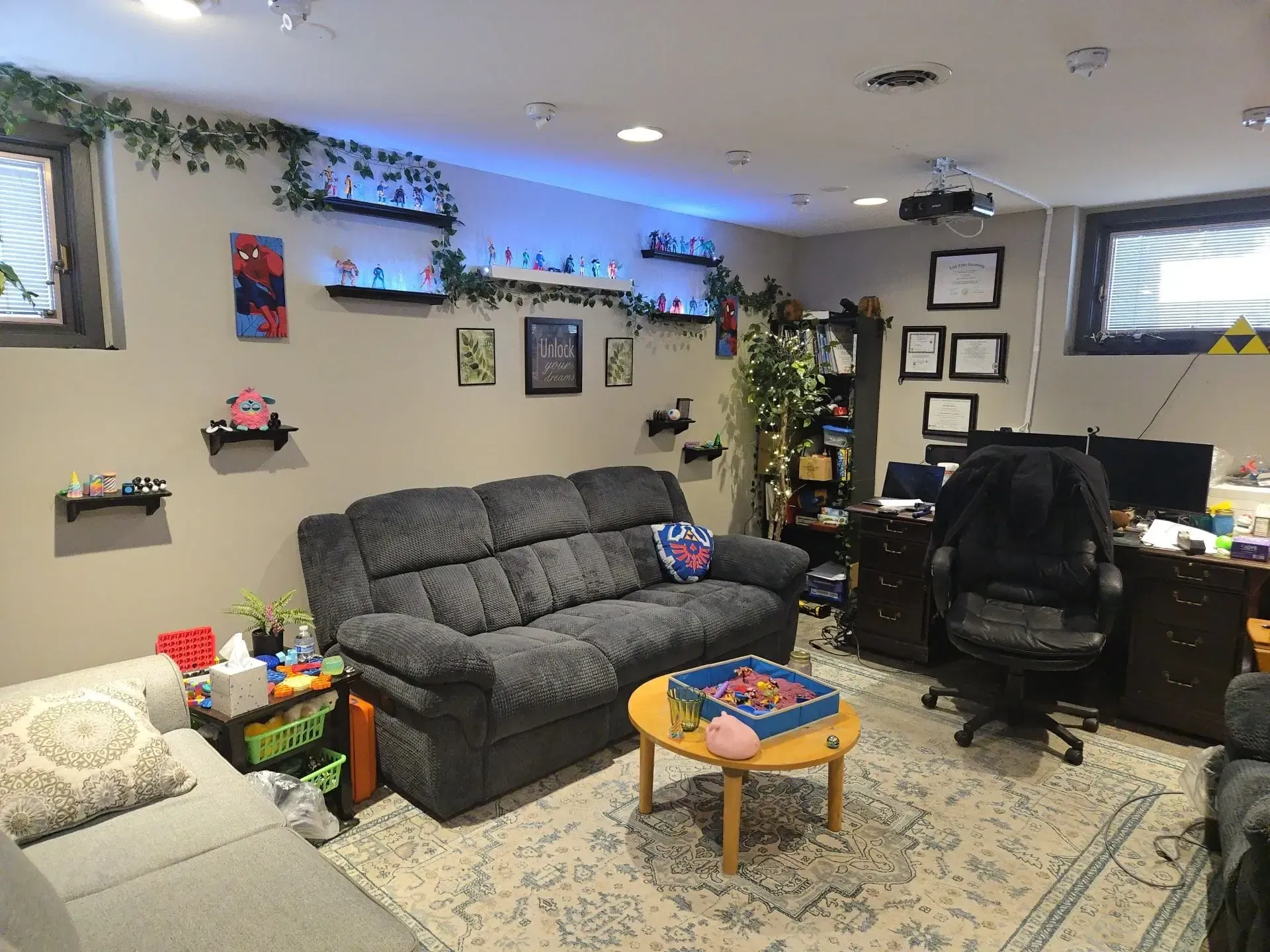 A cozy basement living room with two grey sofas, a coffee table, and walls decorated with shelves, plants, and pictures.