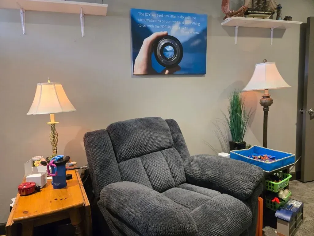 A cozy sitting area features a grey textured recliner flanked by two lamps, with a wall art print displayed above it.