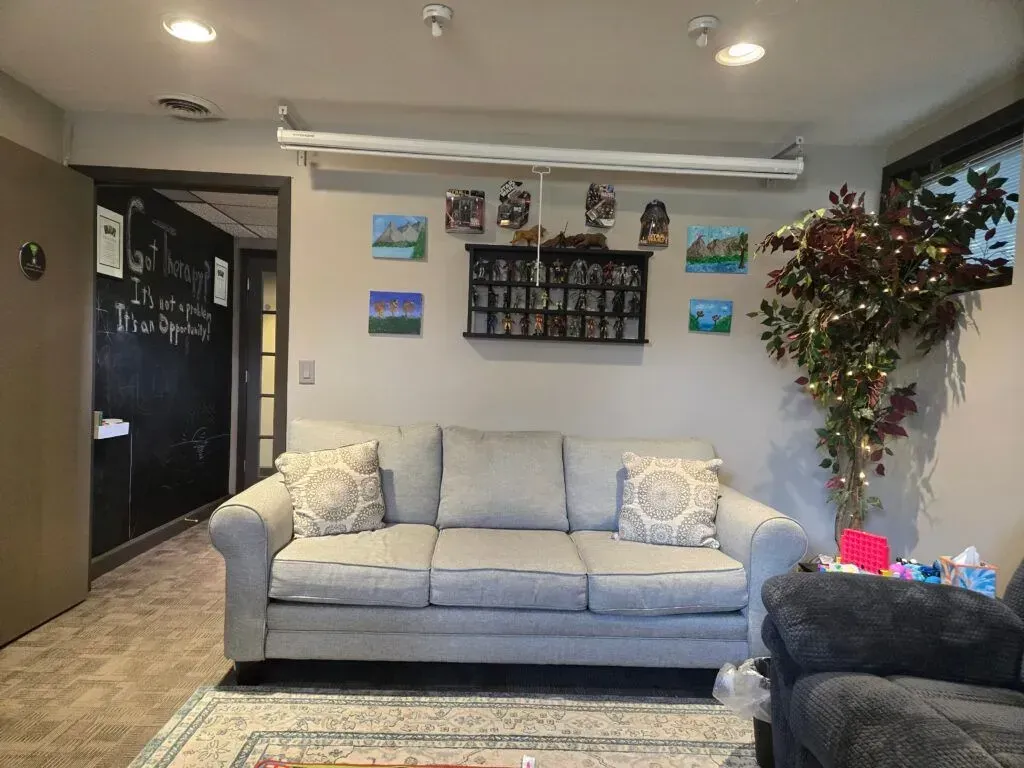 A gray sofa sits centered in a room with a chalkboard wall on the left, a wall-mounted projector screen, and a lit tree.