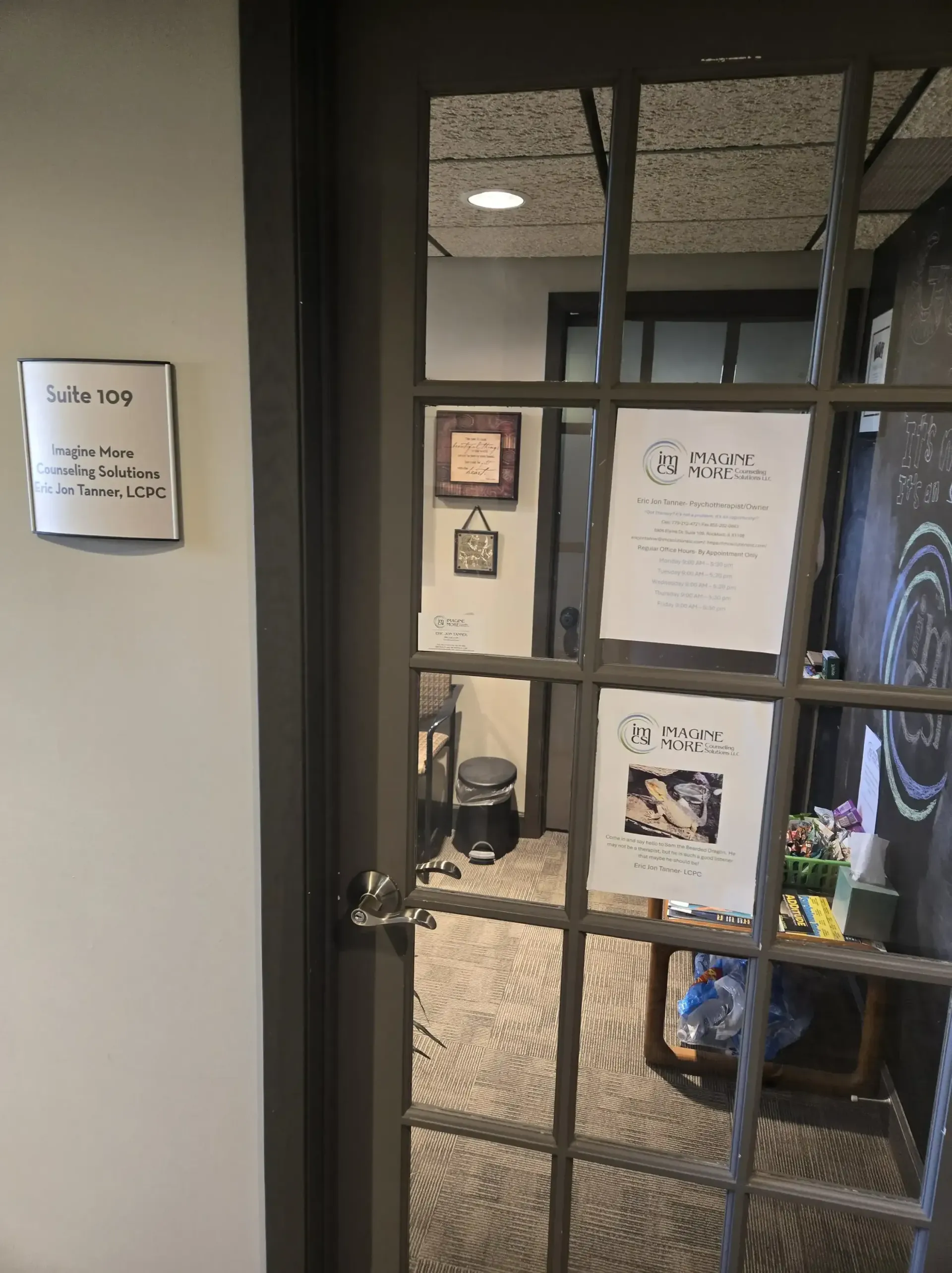 A glass-paned office door with signage on the wall and door, showing a tidy, carpeted interior with a desk and decor.