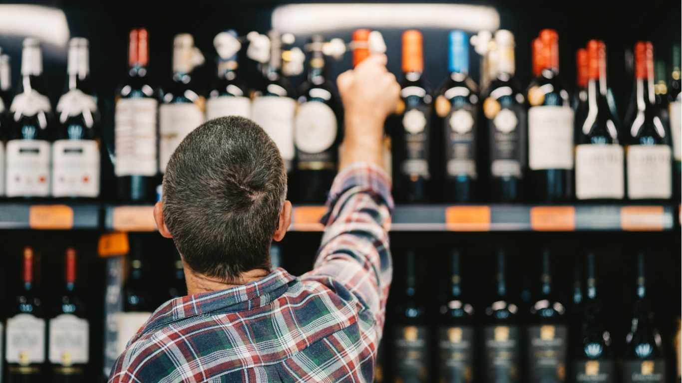 Person reaches for a bottle of wine in a store. Bottles line shelves, dark setting.