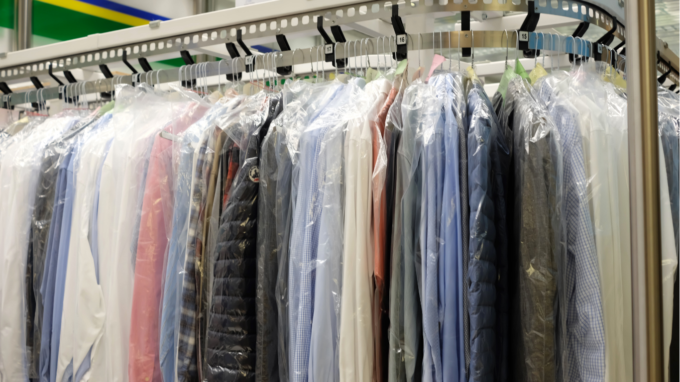 Clothing in plastic covers hanging on a rack at a dry cleaner.