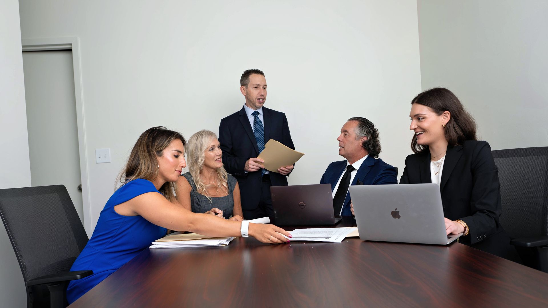 A group of people are sitting around a conference table with laptops.
