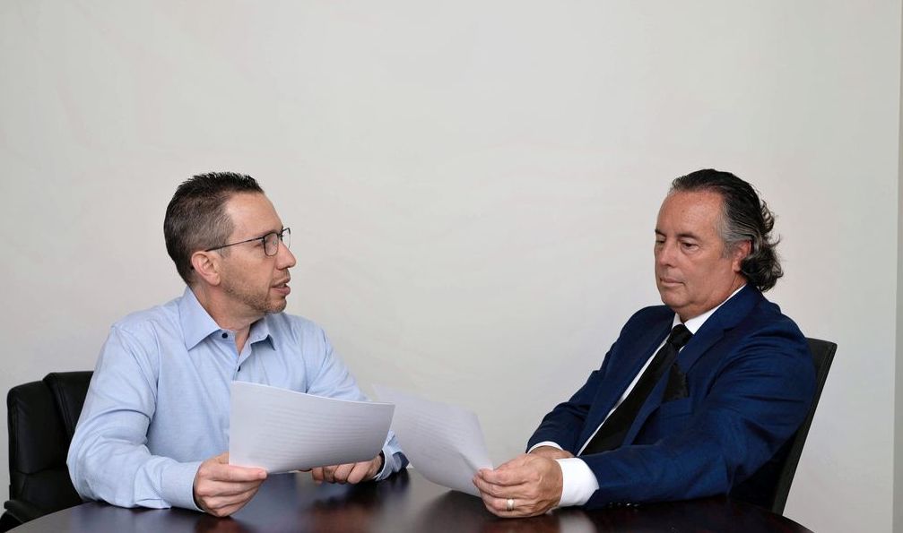 Two men are sitting at a table looking at papers.