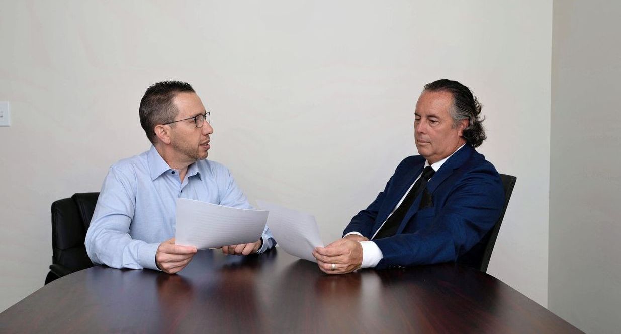 Two men are sitting at a table looking at a piece of paper.