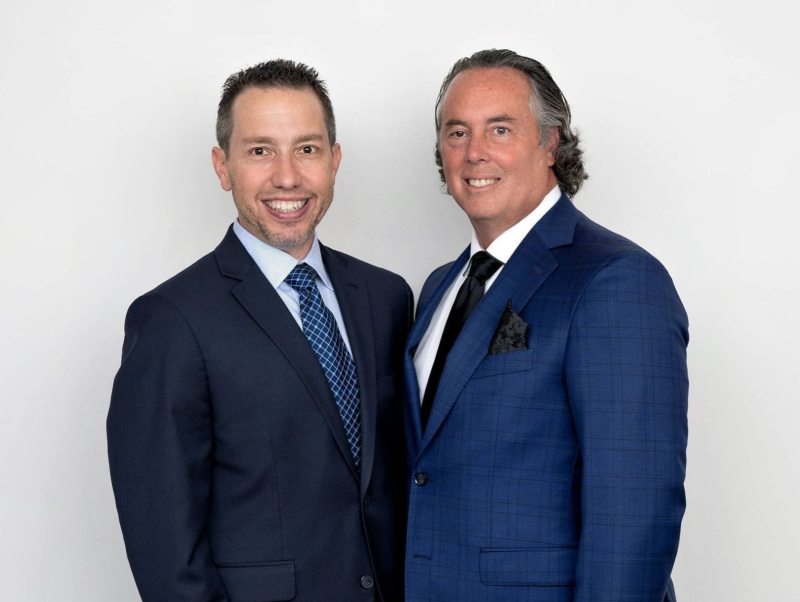 Two real estate attorneys in suits and ties are standing next to each other and smiling.