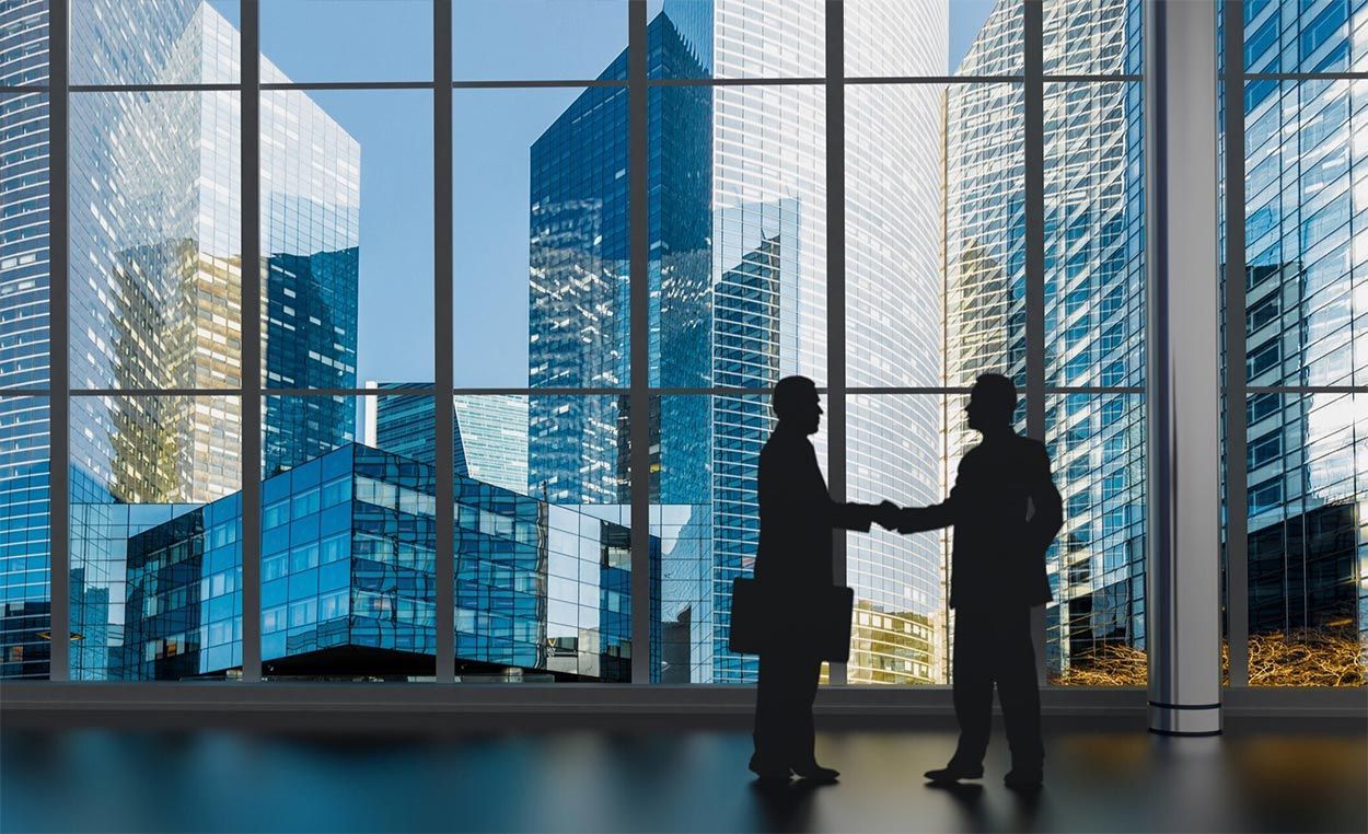 Two men are shaking hands in front of a window with a city skyline in the background.